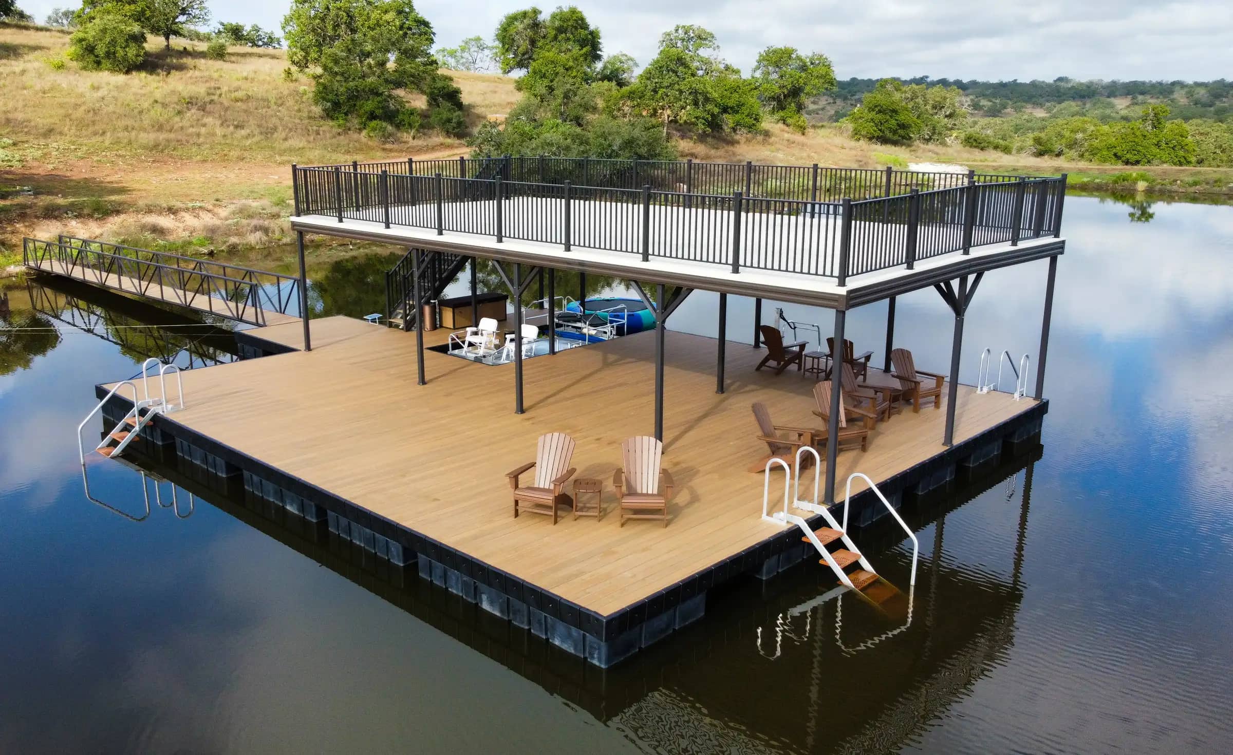 Aerial view of a black-framed aluminum floating dock with composite decking and Adirondack chairs on a Texas Hill Country lake