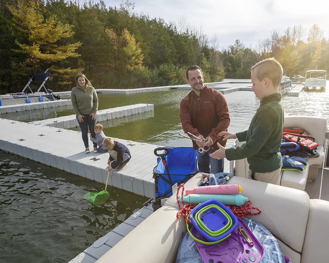 A family out on an EZ Dock floating walkway on an autumn lake, one boy netting from the deck and another handing over a fishing rod