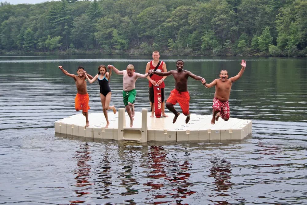 Six people jumping off a plain EZ Dock floating platform into a wooded lake