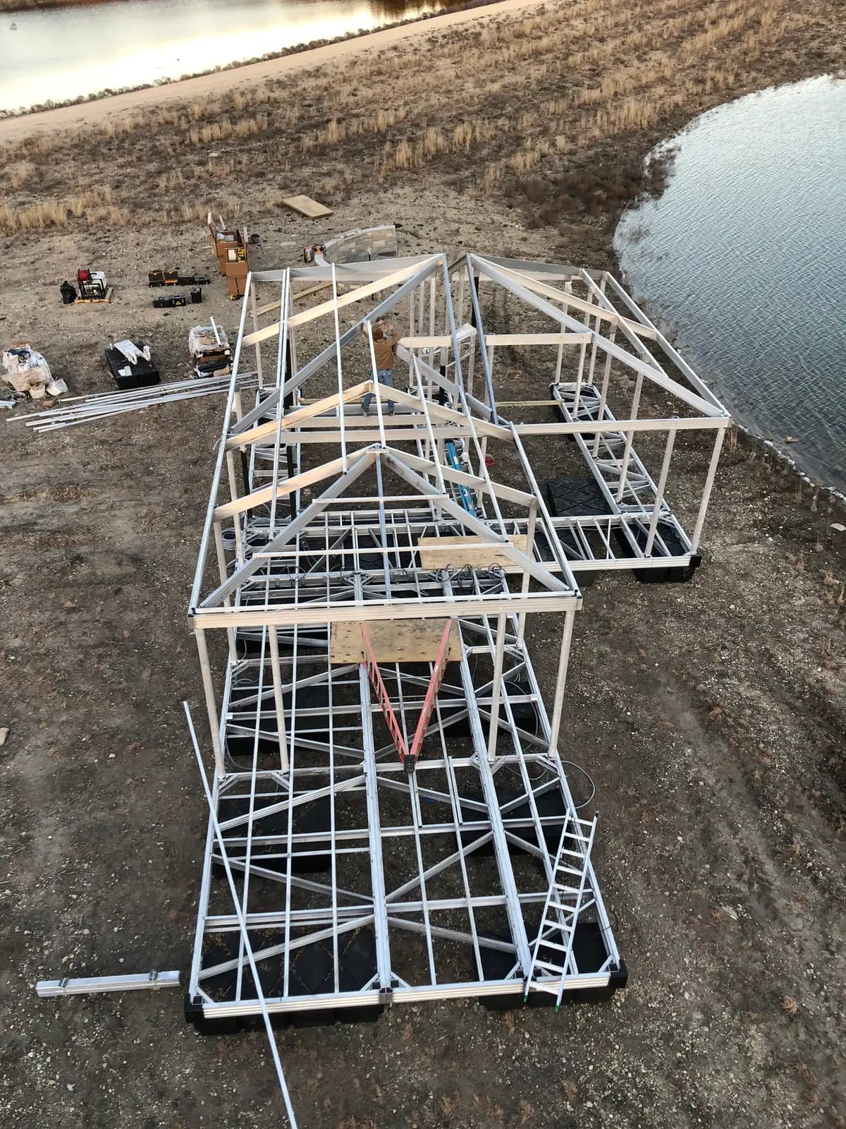 Aerial view of an aluminum dock frame assembled on the bank beside a pond, before it is set on the water.