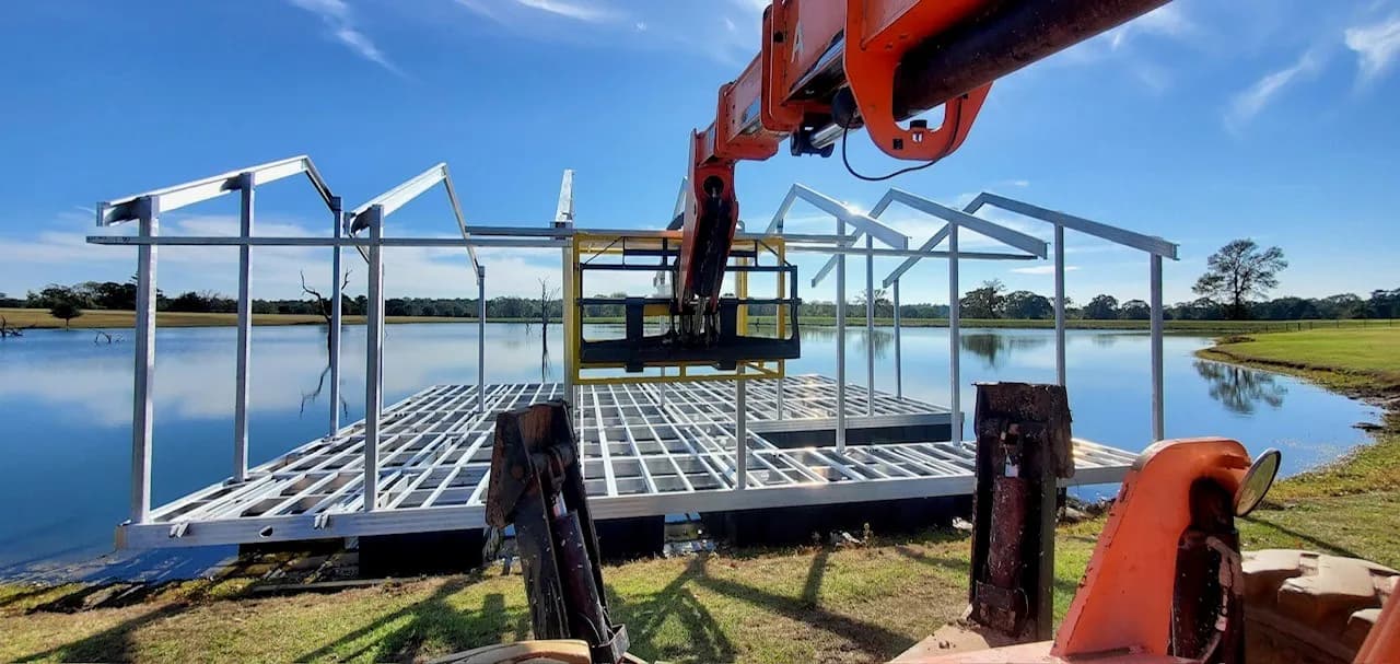A telehandler working an aluminum dock frame that floats on the water, moving it into position during an install.