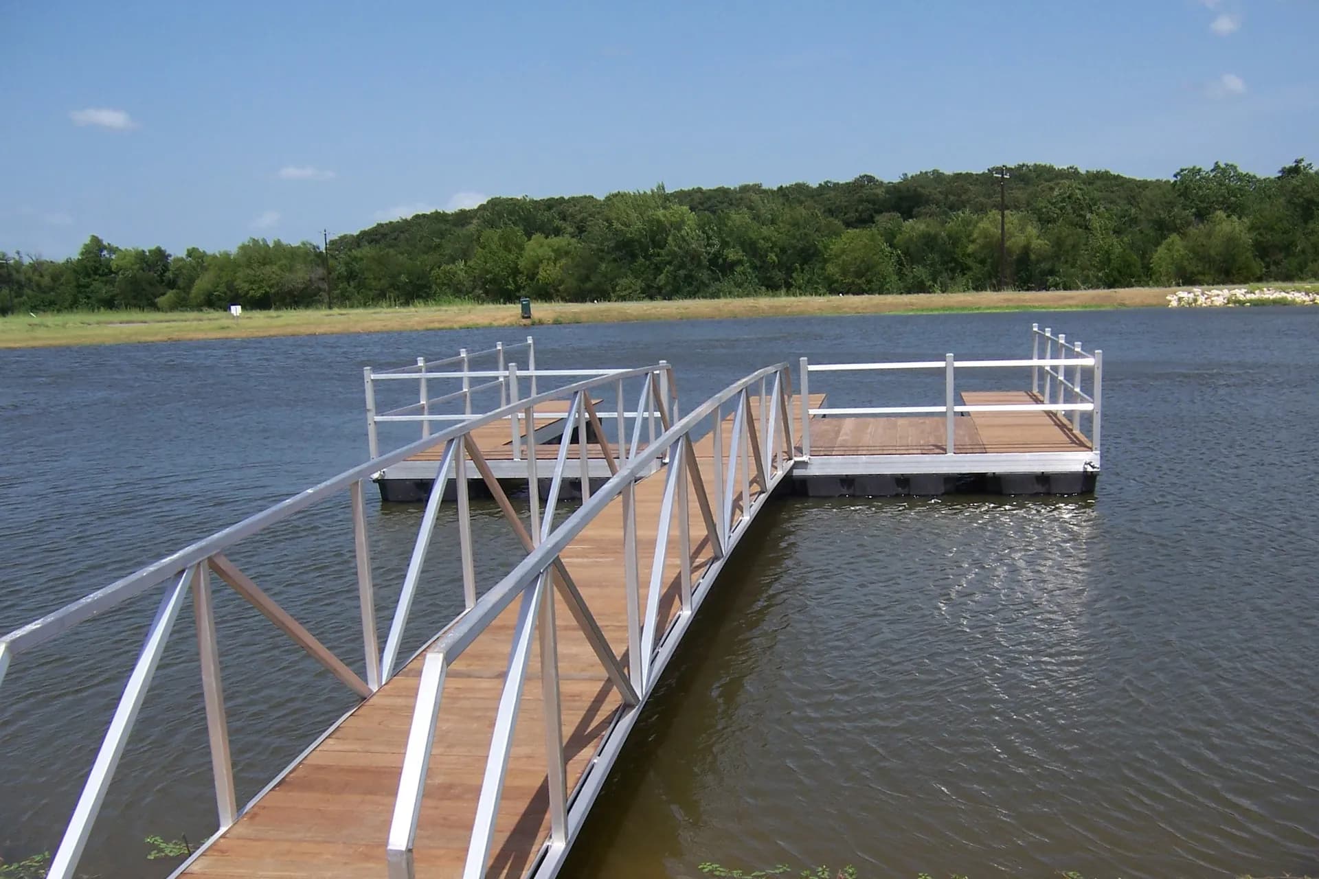 Aluminum gangway leading out to an open floating dock with railings over calm water.