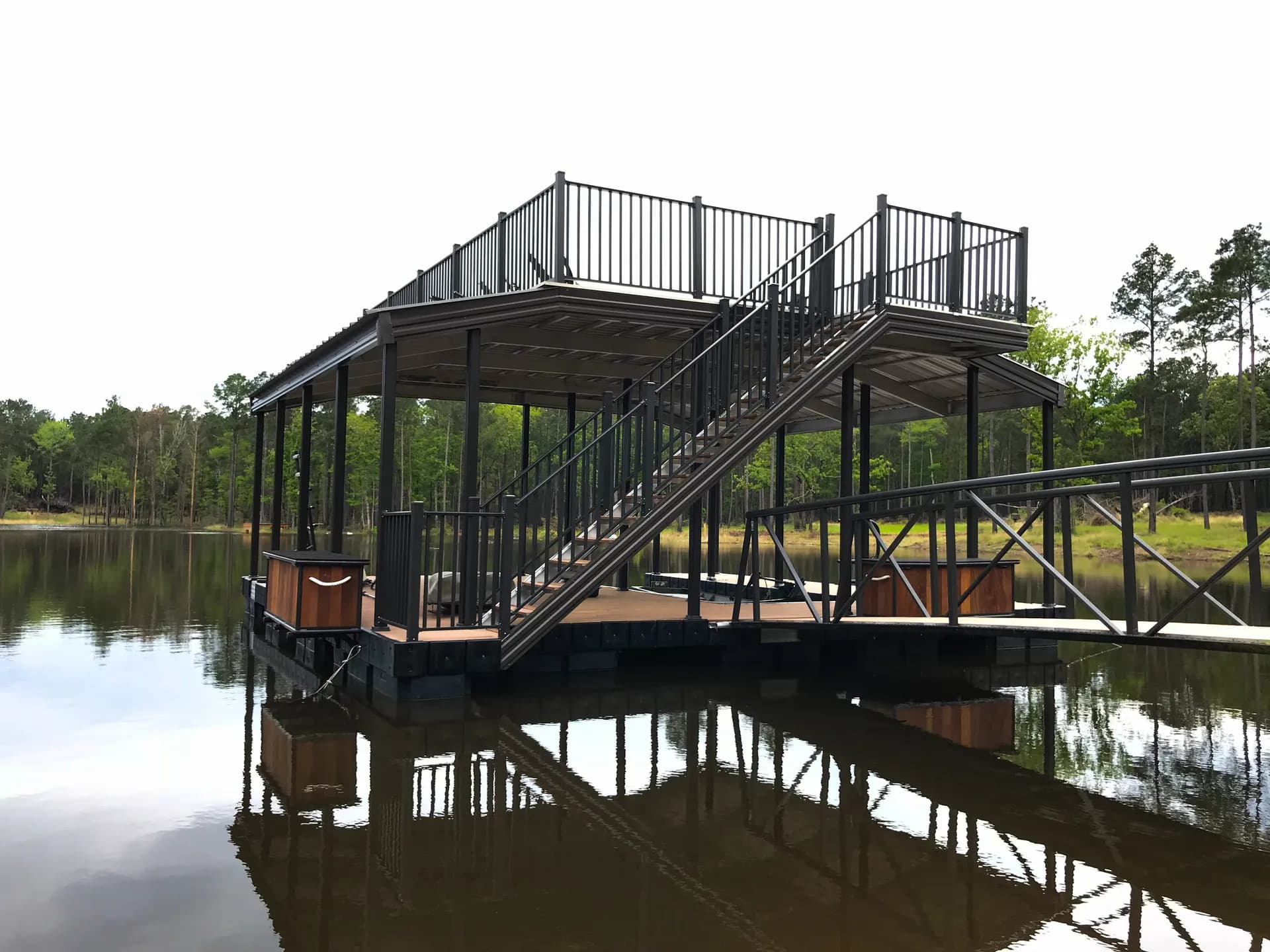 A black two-story covered aluminum dock with an upper sun deck, mirrored on dark, calm water.