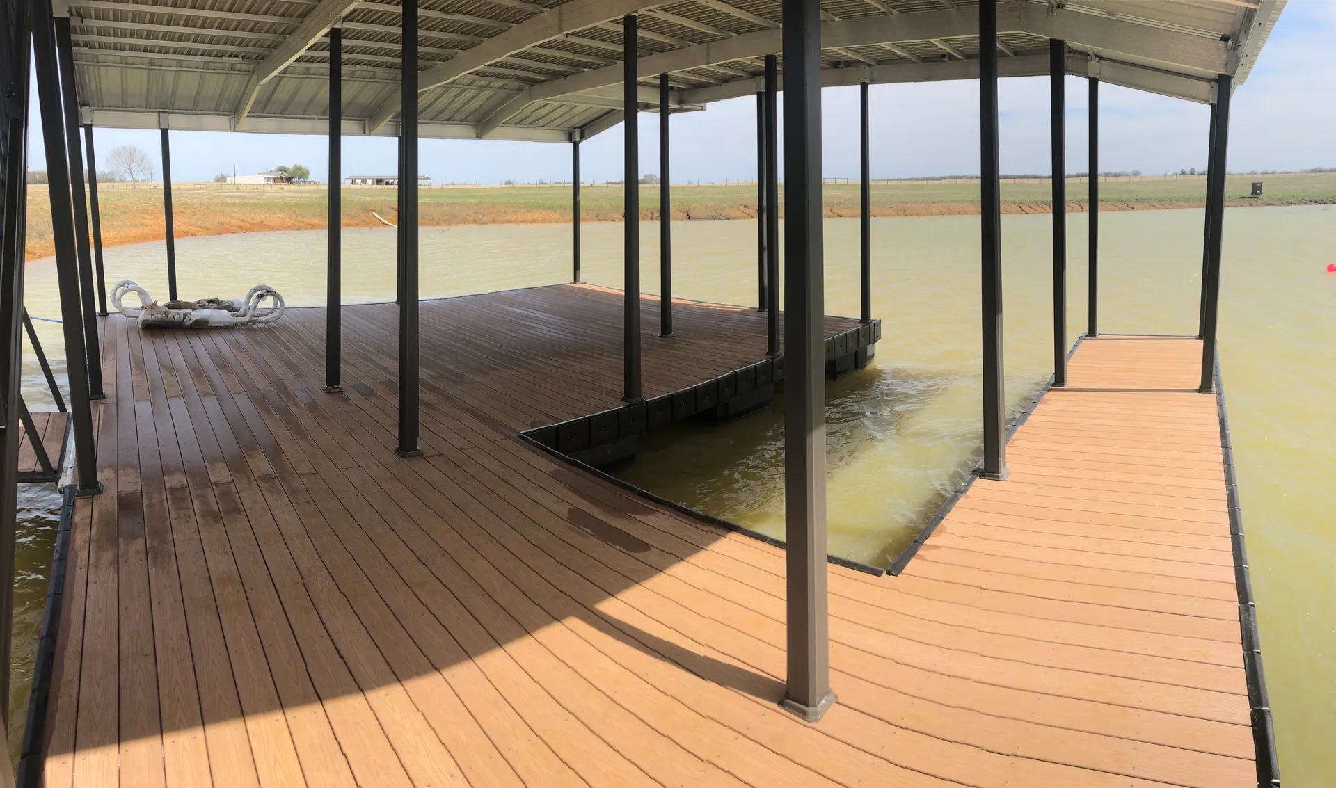 Under a covered aluminum dock: wide composite decking, painted posts, and a ramped gangway down to the water.