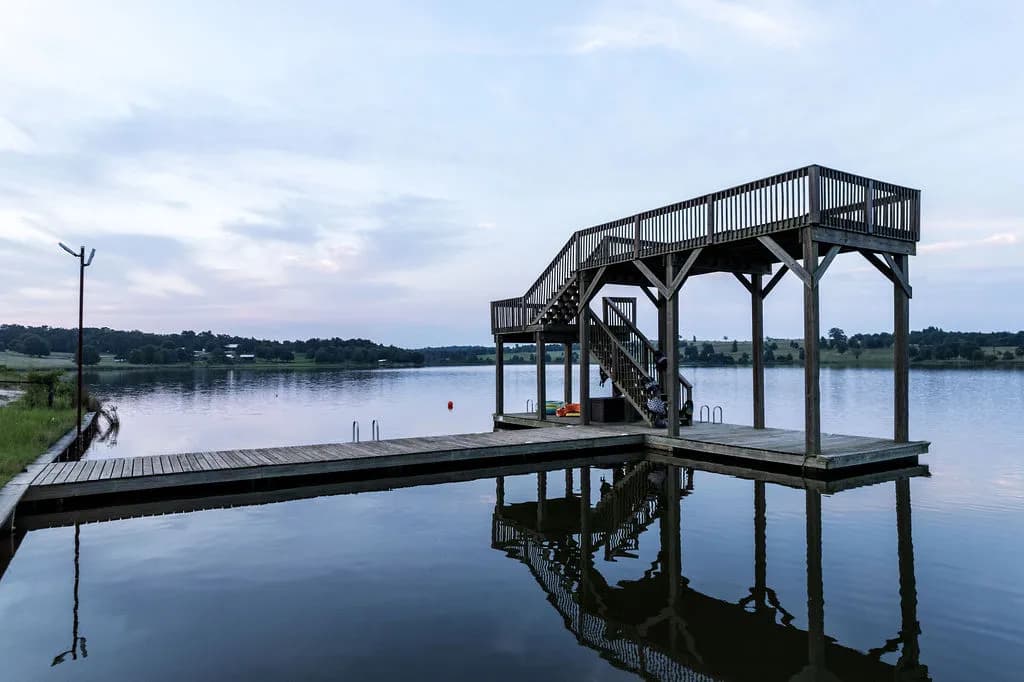 Covered aluminum dock with an upper sun deck mirrored in a still lake at midday.