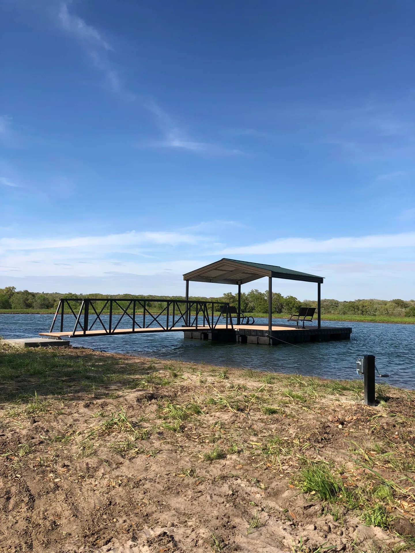 Covered aluminum boat dock with a hip roof and a gangway reaching a sandy bank.