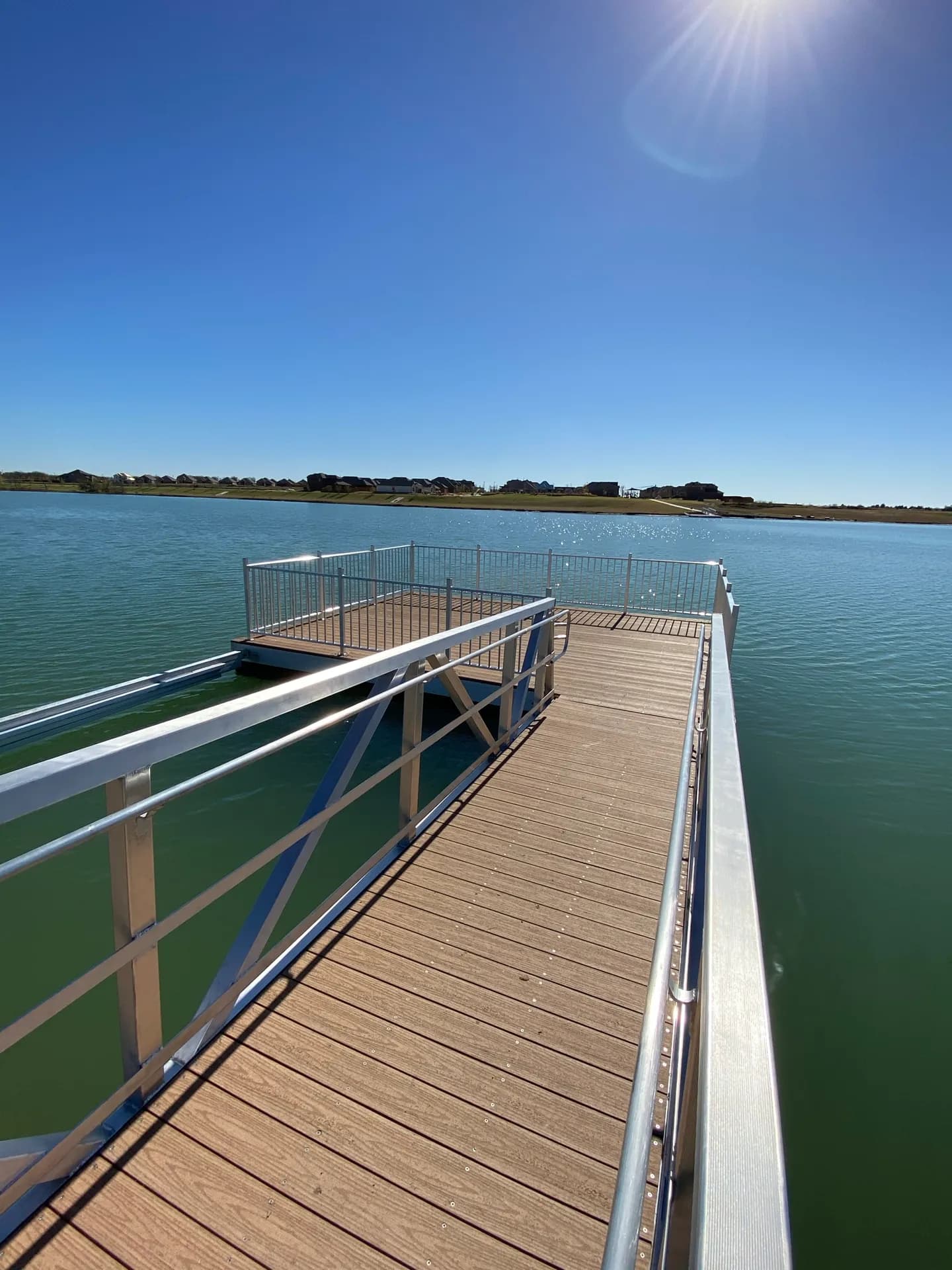 Brown composite dock decking and an aluminum gangway meeting the shoreline on a clear lake.