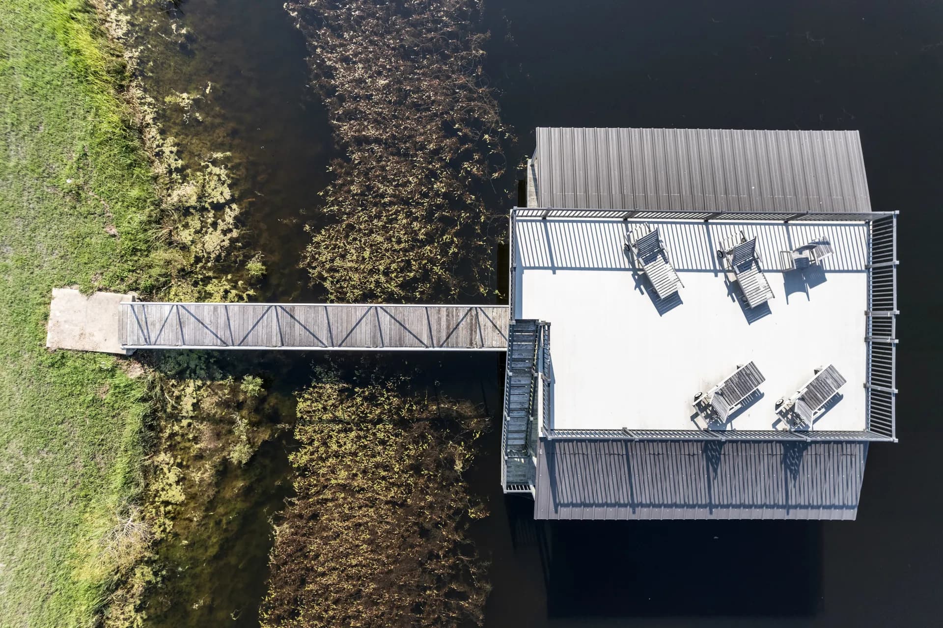 Overhead view of an aluminum covered dock and gangway with a furnished sun deck on a green pond.