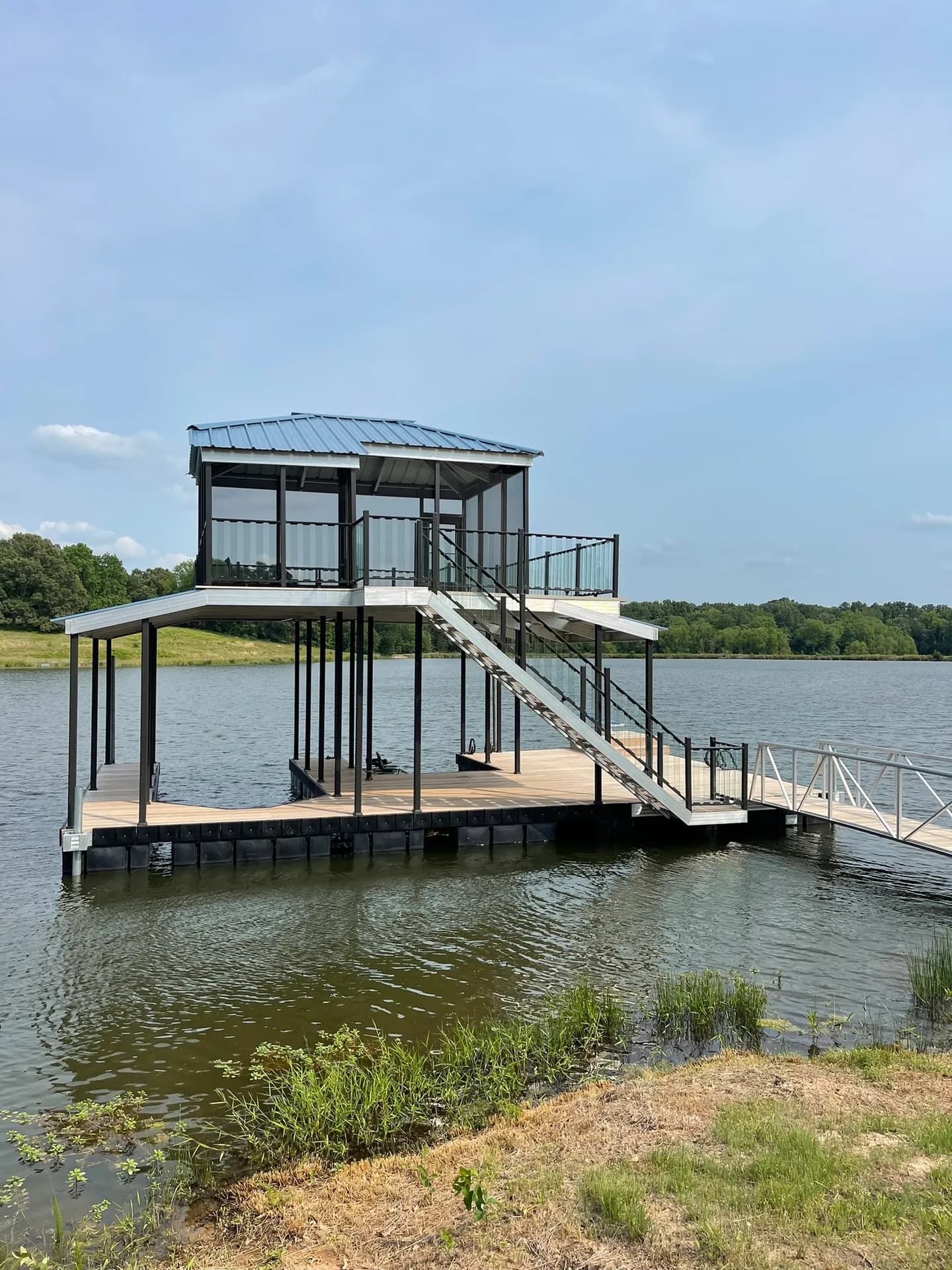 Two-story covered aluminum dock with an upper sun deck and a gangway reaching a sandy bank.