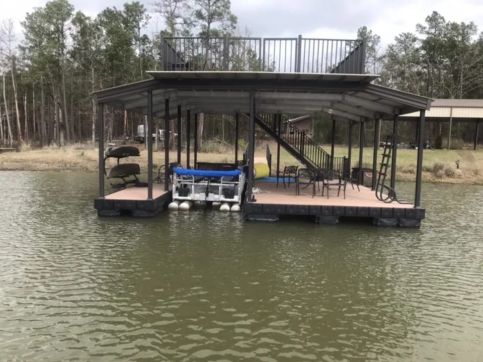 Two-story covered aluminum dock with a dark frame and railed upper sun deck, viewed across the water from the front.