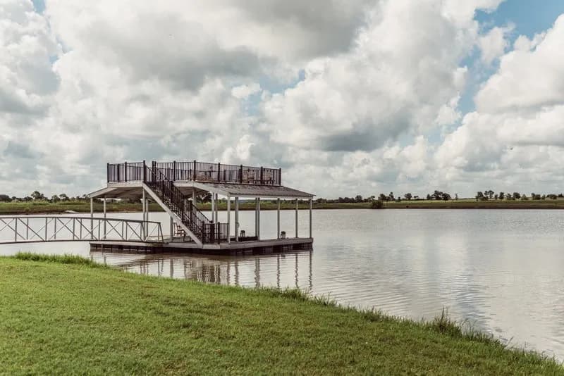 Two-story covered dock with an aluminum walkway from a mowed grass bank, under a wide cloudy sky over calm water.