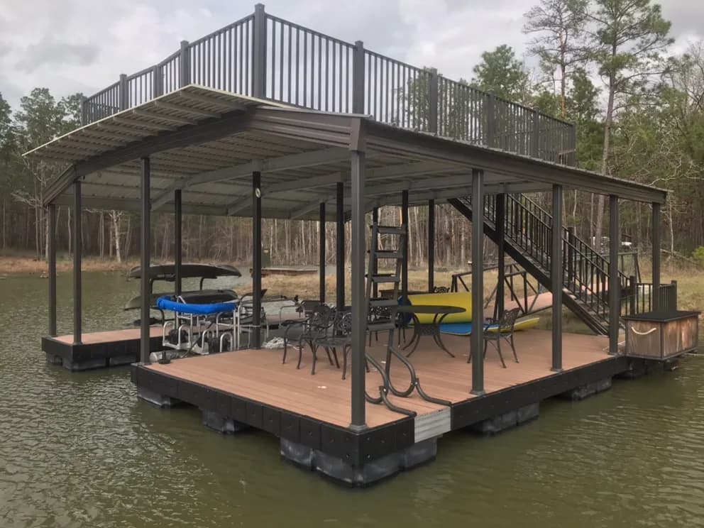 Close view of a two-story covered aluminum dock with a furnished lower deck, a boat lift, and stairs up to a railed sun deck.